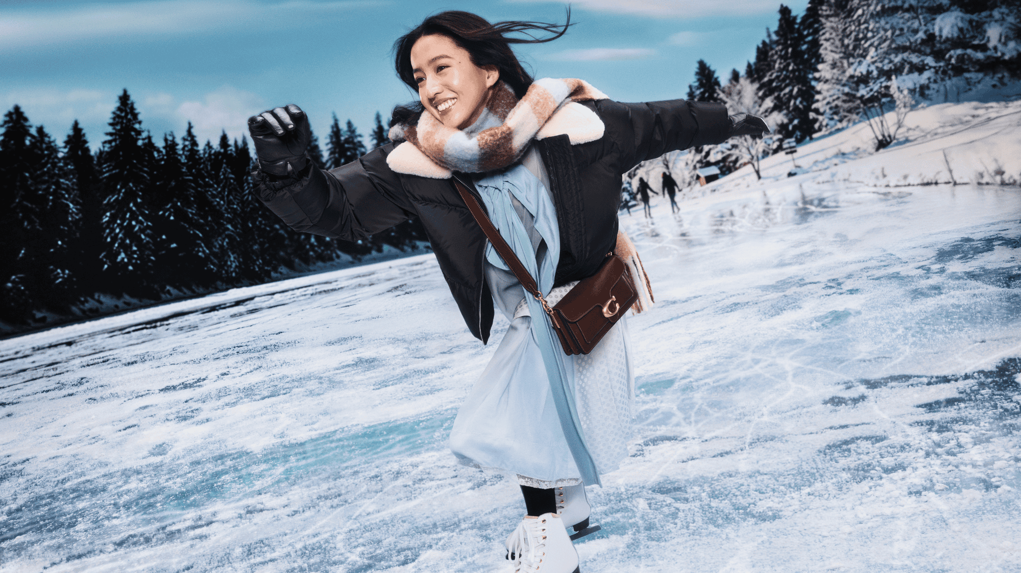 Woman in a snowy landscape with trees and a clear sky carrying a coach bag